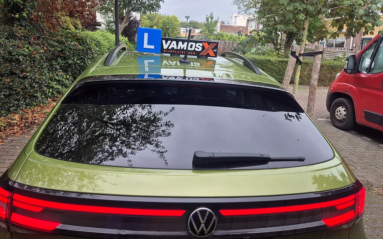 Achterkant van onze groene Volkswagen schakel-lesauto met het VamosX-dakbord en L-blok