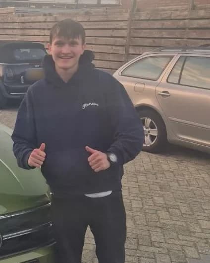 Sven, trots met duim omhoog naast de groene schakel-lesauto na het behalen van zijn rijbewijs