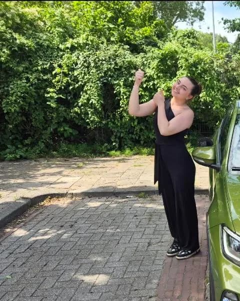 Tina, trots naast de groene schakel-lesauto na het behalen van haar rijbewijs